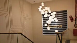 A modern staircase with glass railings, a geometric wall pattern, and a unique hanging light fixture. - Hotel Phantom (Ganganagar)
