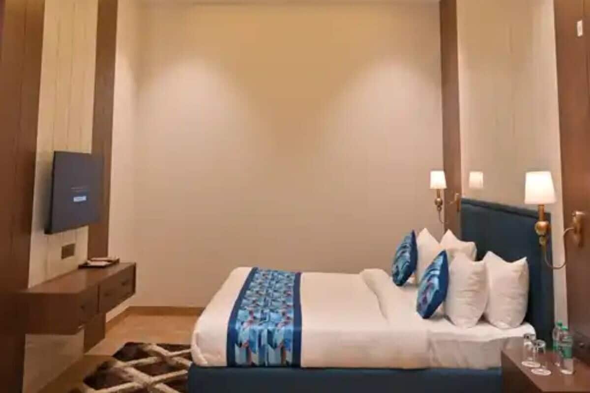 A modern hotel room with a neatly made bed, a flat-screen TV on a wooden console, and a ceiling with recessed lighting.