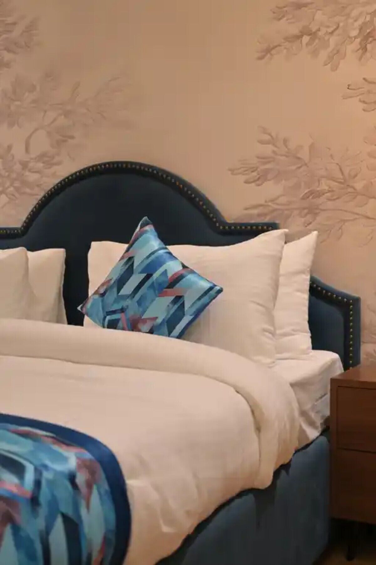 A bed with a dark headboard, white pillows, and a colorful throw blanket.