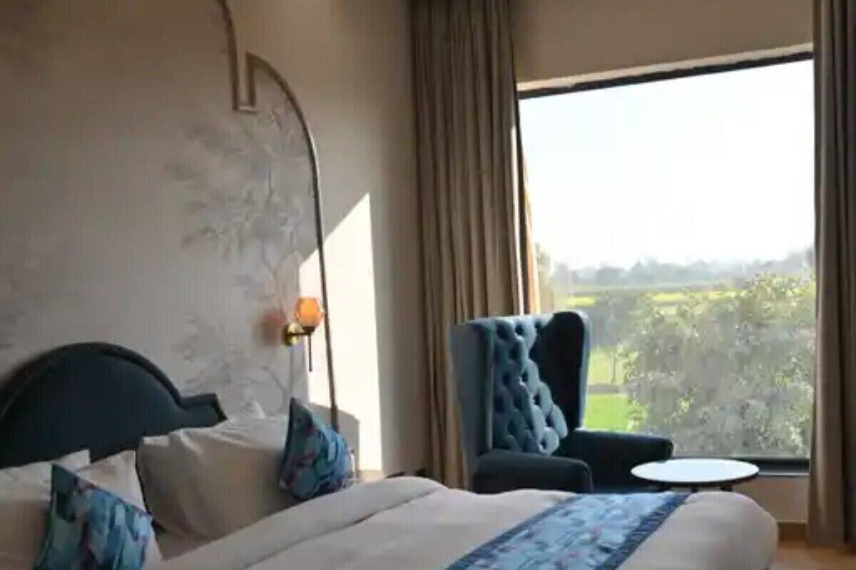 A modern hotel room with a large bed, a chair, a small table, and a view of the outdoors.