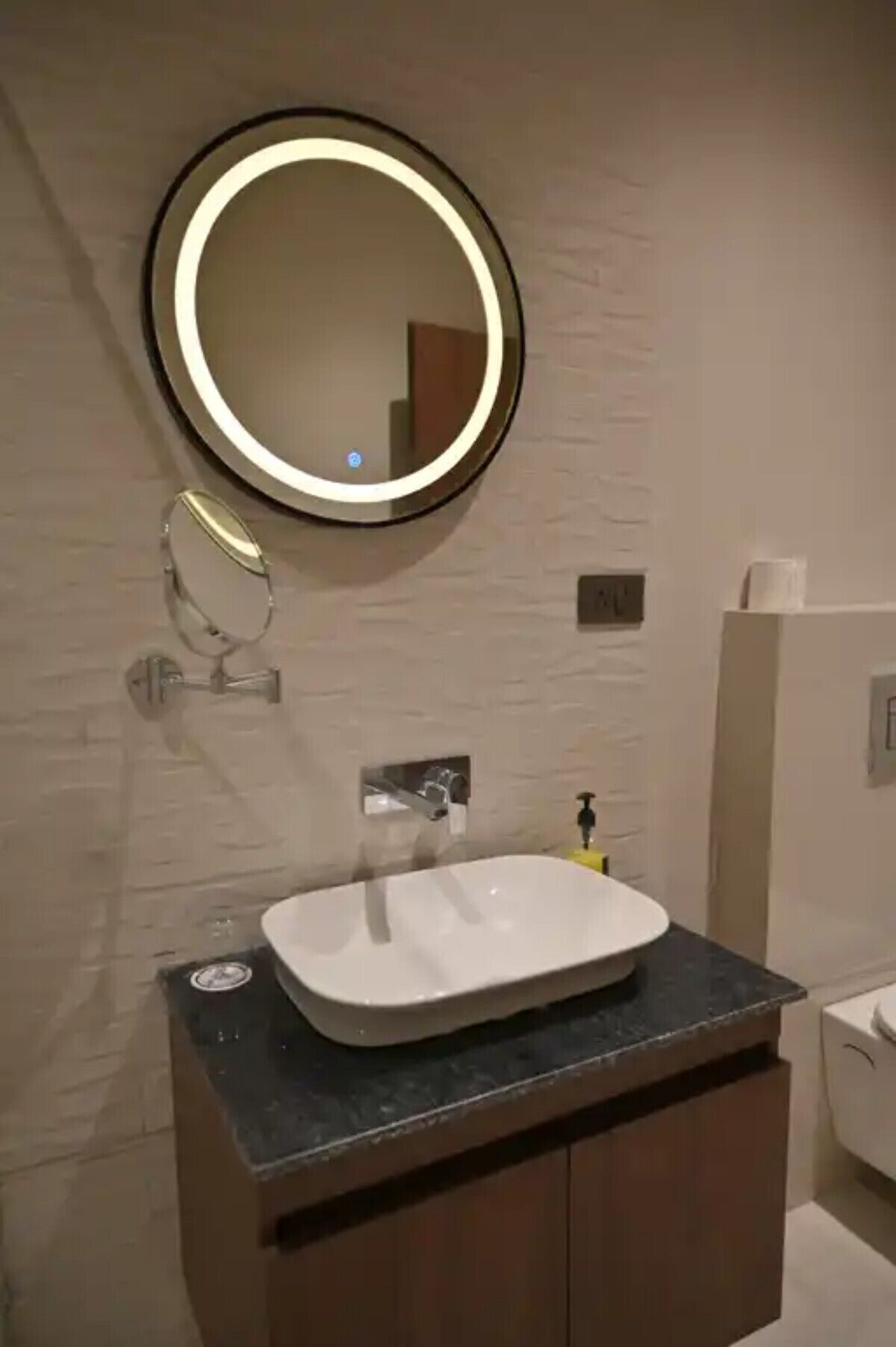 A bathroom with a round mirror, a white sink, and a toilet.