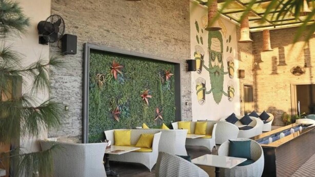 An outdoor seating area with wicker furniture, a green wall with decorative elements, and a patterned floor. - Hotel Phantom (Ganganagar)