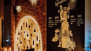 A cozy bar area with brick walls, a large mural of beer ingredients, and a seating arrangement with chairs and a bar counter. - Hotel Phantom (Ganganagar)