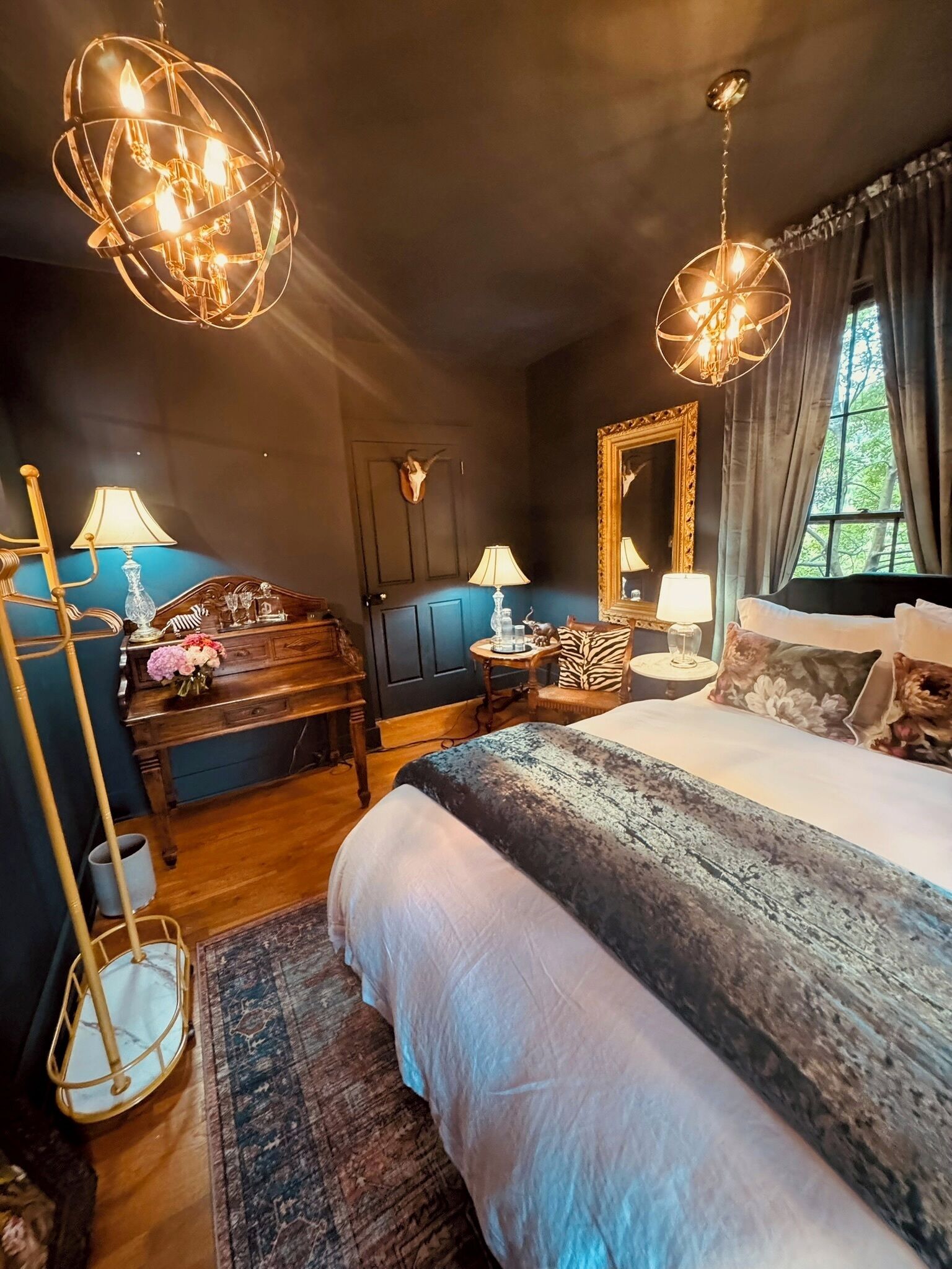 A bedroom with a large bed, two bedside tables, a dresser, a mirror, and two hanging light fixtures.