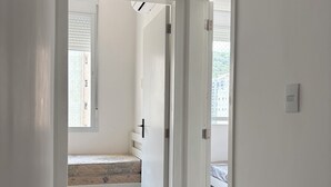 A narrow hallway with a door leading to a room with a bed and a window.