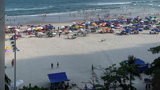 A beach with umbrellas and people, a clear sky, and buildings in the background.