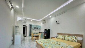 A modern bedroom with a large bed, a small kitchenette, and a bathroom with a glass shower. - AP Home (Ho Chi Minh City)