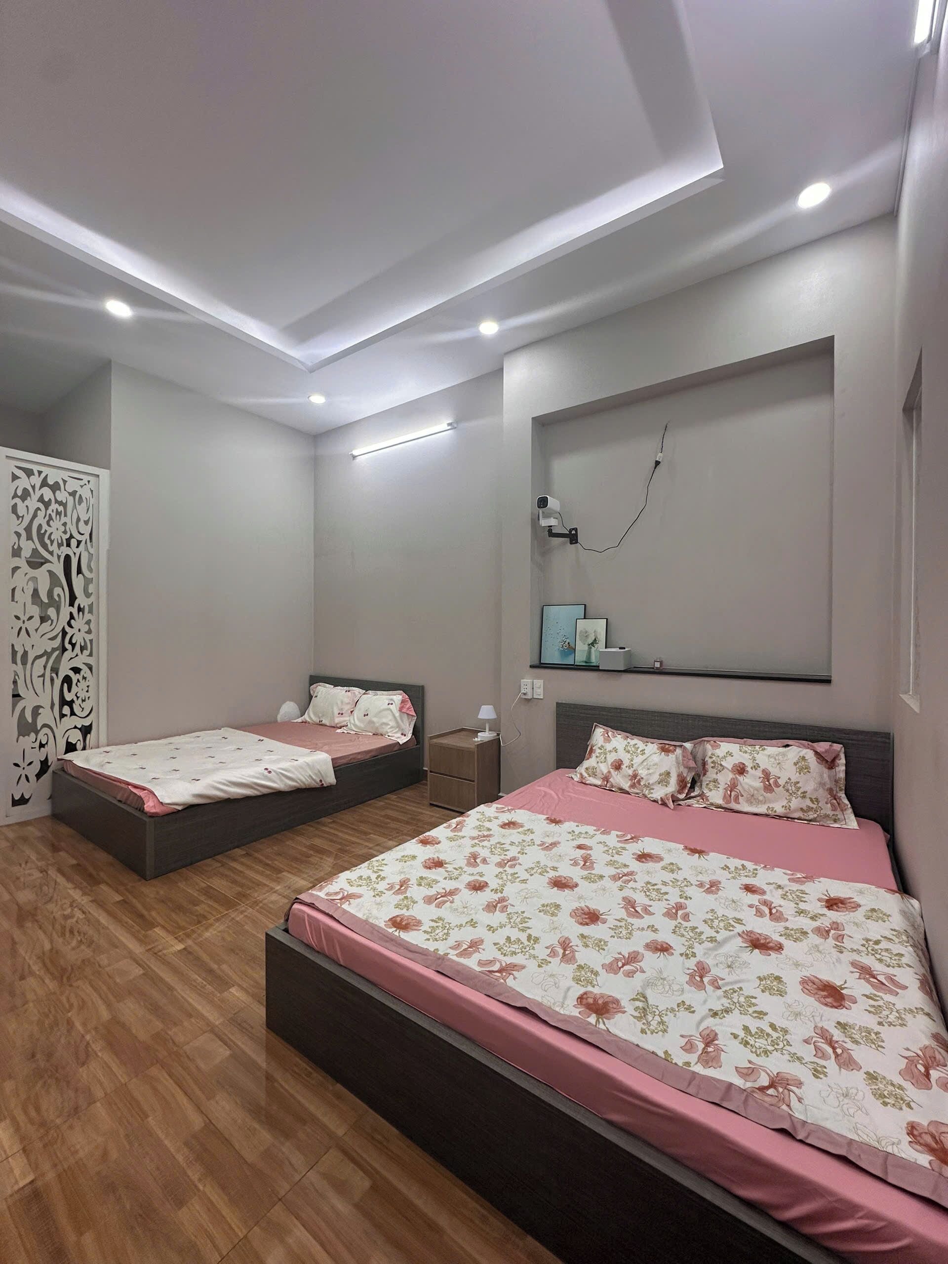 A modern bedroom with two beds, a wooden floor, and recessed ceiling lighting.