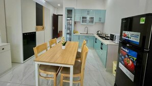 A modern kitchen with light blue cabinets, a black refrigerator, and a wooden dining table with chairs. - AP Home (Ho Chi Minh City)
