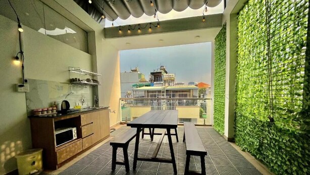 A modern kitchen with a dining area, a green wall, and a view of buildings. - AP Home (Ho Chi Minh City)