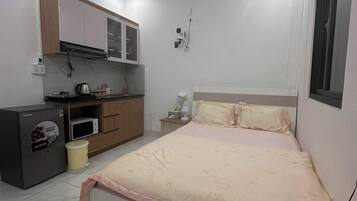 A bedroom with a bed, a bedside table, a nightstand, a wardrobe, a built-in microwave, and a refrigerator.