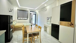 A compact, well-lit room with a dining table, chairs, a bed, a kitchenette, and a wardrobe. - AP Home (Ho Chi Minh City)