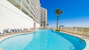 A swimming pool with lounge chairs and a building with balconies. - Lighthouse 1211, Spacious Beachfront Condo, Sleeps 8, 3 pools.  Owner managed. (Gulf Shores)