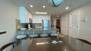 A modern kitchen with white cabinets, a central island with seating, and a large chandelier. - Lighthouse 1211, Spacious Beachfront Condo, Sleeps 8, 3 pools.  Owner managed. (Gulf Shores)