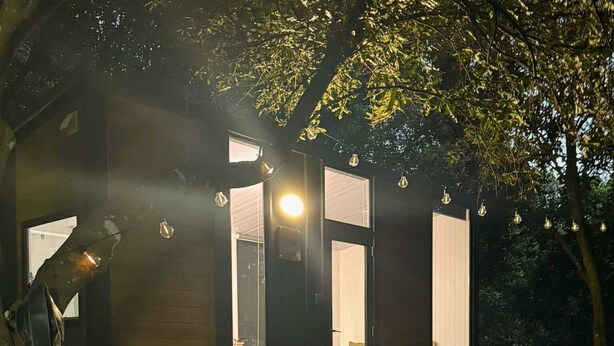A modern, compact cabin with a wooden deck and a staircase leading to a door. - Under the Velvet Sky by Tiny Away (Dagun)