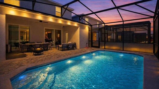 A swimming pool with a glass enclosure, surrounded by a patio area with outdoor furniture. - 5BR 5BA Luxury Villa Private Pool Resort - WCA (Clermont)