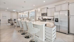A modern kitchen with white cabinetry, stainless steel appliances, and a central island with bar stools. - 5BR 5BA Luxury Villa Private Pool Resort - WCA (Clermont)