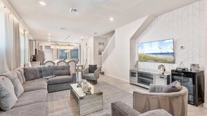 A spacious living room with a sectional sofa, a coffee table, and a large flat-screen TV mounted on the wall. - 5BR 5BA Luxury Villa Private Pool Resort - WCA (Clermont)