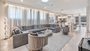 A spacious living room with a grey sectional sofa, a coffee table, and a dining area with a table and chairs. - 5BR 5BA Luxury Villa Private Pool Resort - WCA (Clermont)