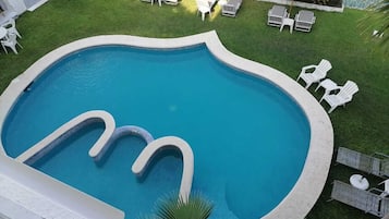 Ein Pool mit außergewöhnlichem Design, umgeben von weißen Liegestühlen und Sonnenschirmen, vor einer gepflegten Rasenfläche.