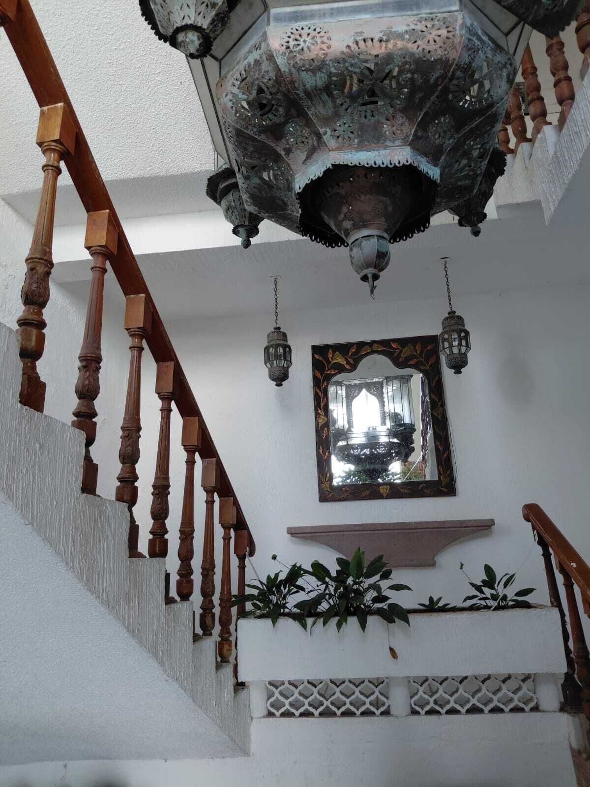 A staircase with wooden balusters, a decorative ceiling light fixture, a wall-mounted mirror, and potted plants.