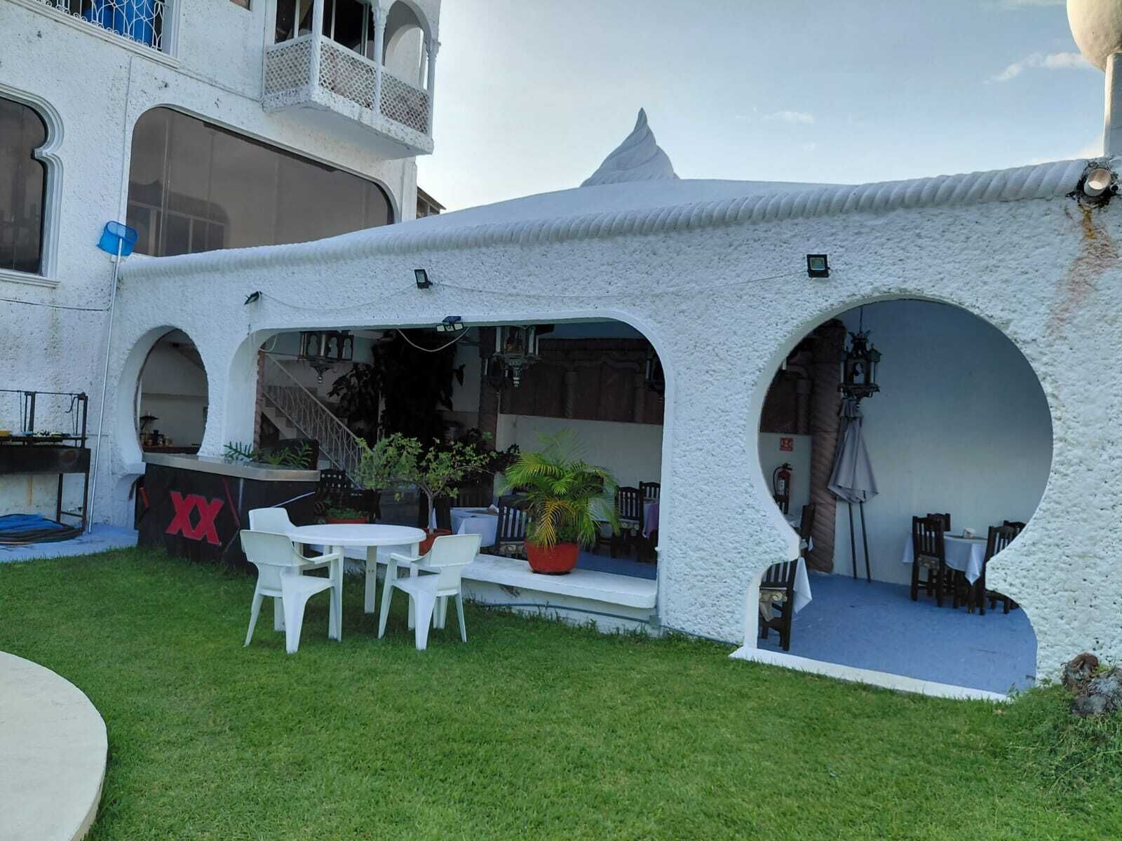 Une cour avec un espace abrité par une tente blanche, des sièges en plein air et un escalier menant à un niveau supérieur.