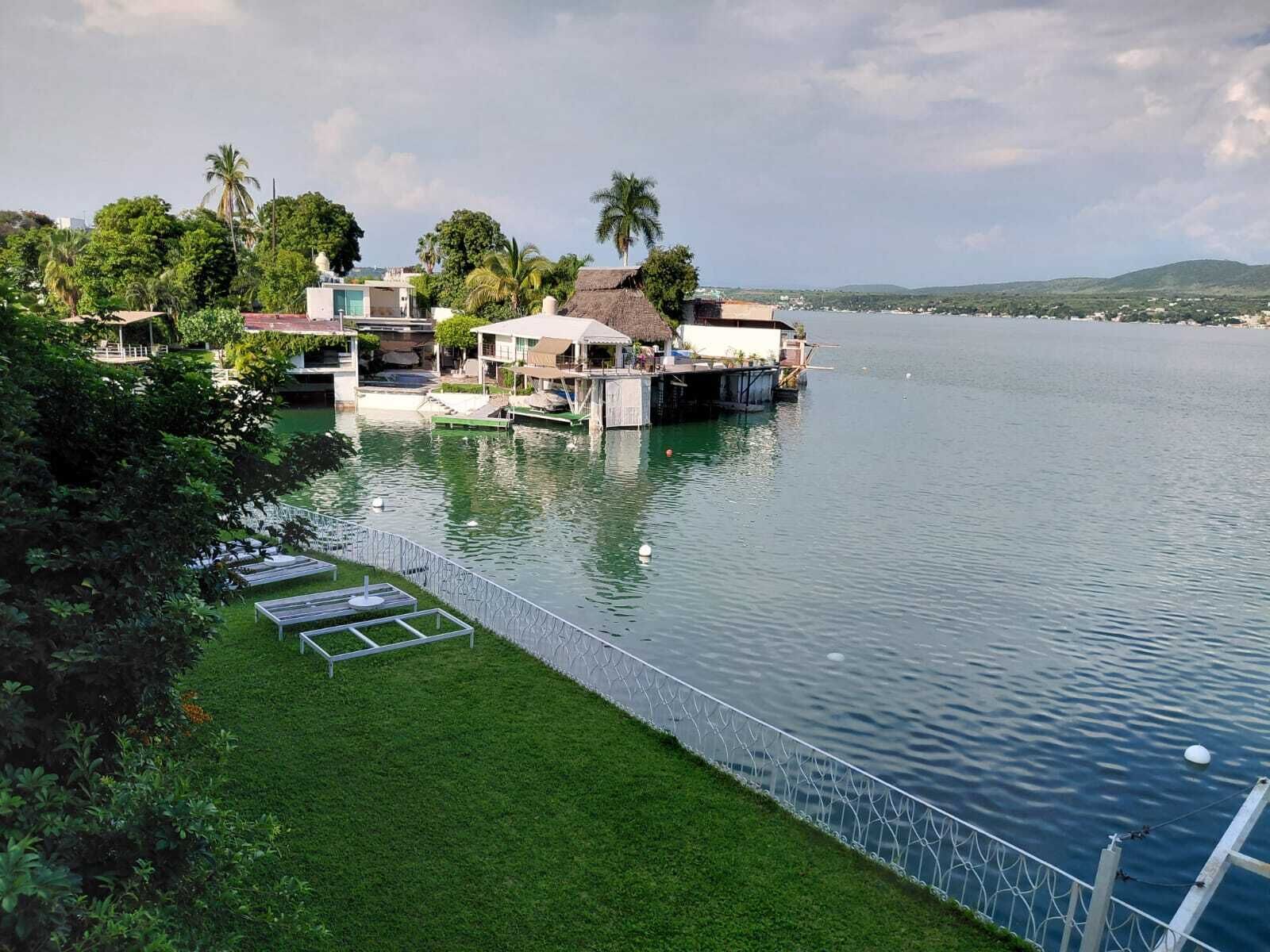 Una propiedad junto al lago con estructuras flotantes, un espacio verde con valla y una vista despejada del agua.