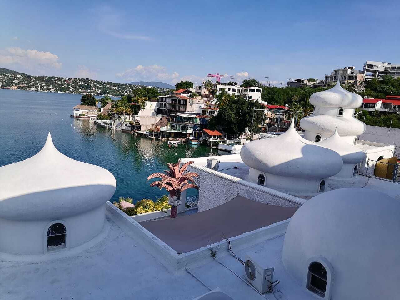 A coastal view with white domed buildings, a marina, and a distant town.