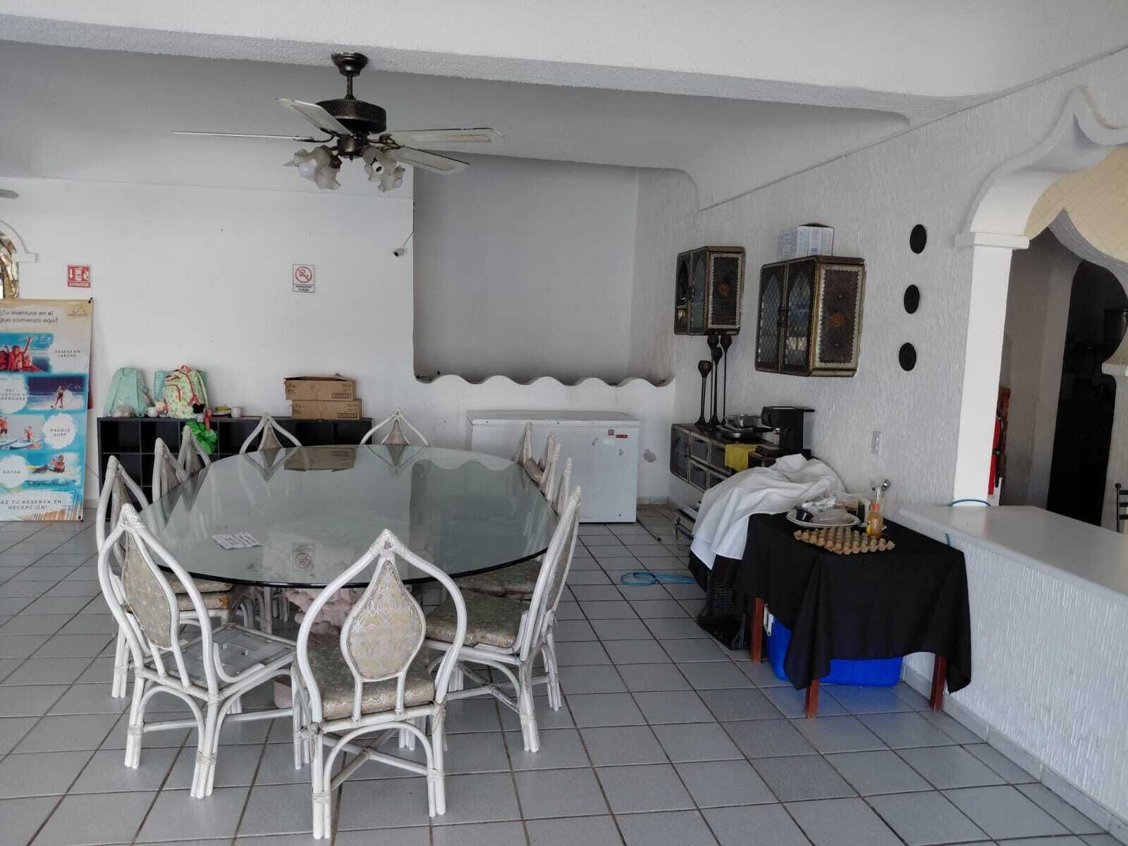 A dining area with a round glass table and white wicker chairs, a ceiling fan, and a white wall with a decorative archway.