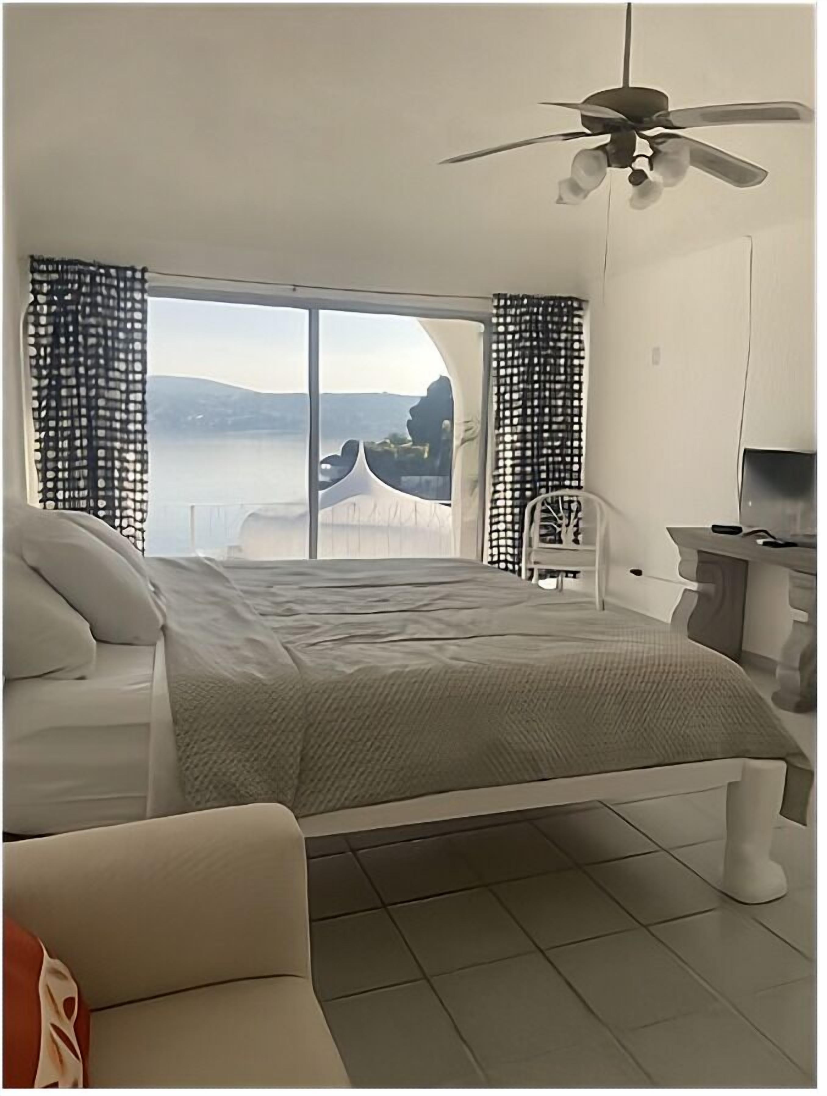 A bedroom with a bed, a chair, a TV, and a view of the sea.