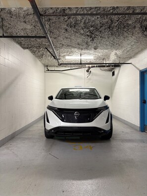 A white car parked in a parking garage with white brick walls and a blue door. - Amazing Views, Close to Football Stadium, Cruiseliners (Vancouver)
