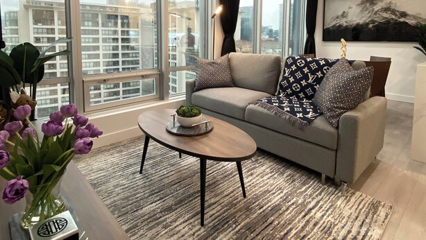 A modern living room with a grey sofa, a coffee table, and a large window offering a city view. - Amazing Views, Close to Football Stadium, Cruiseliners (Vancouver)