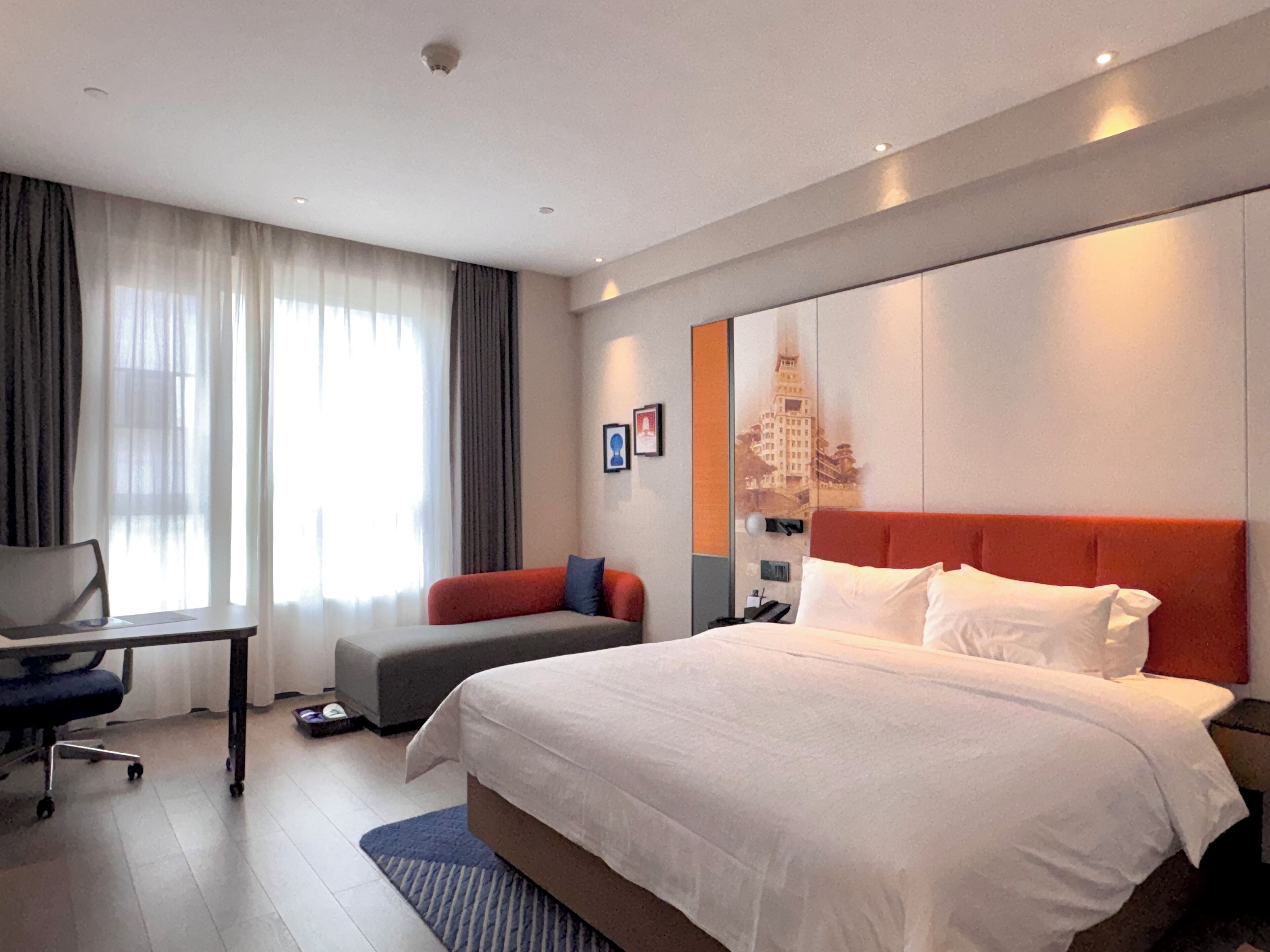 Una camera d'albergo con un letto grande, una scrivania, una sedia, un divano e un'ampia finestra con tende.