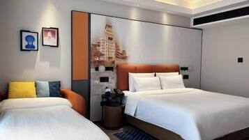 A hotel room with two beds, a nightstand, a trash bin, and a wall with a cityscape painting.