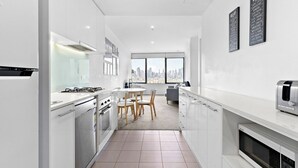 Eine moderne Küche mit weißen Schränken, einem Gasherd, einer Mikrowelle und einem Toaster. Es gibt einen Essbereich mit Tisch und Stühlen sowie ein großes Fenster mit Blick auf die Stadt.