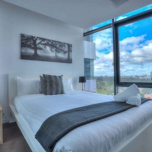 Ein modernes Schlafzimmer mit einem großen Bett, Blick auf die Stadt durch ein Fenster und einem Gemälde an der Wand.