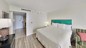 Une chambre d’hôtel comprenant un lit, des tables de chevet, une lampe, une chaise et une porte donnant sur une autre pièce.