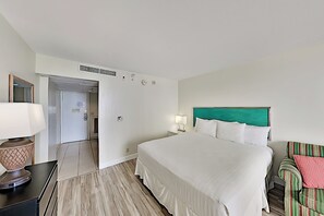 A hotel room with a bed, bedside tables, a lamp, a chair, and a door leading to another room. - Palms Waikiki Studio with Partial Ocean Views (Honolulu)