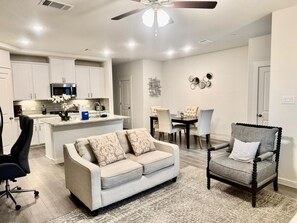 A modern kitchen with white cabinets, a central island, and a dining area with a table and chairs. - FW002 | Ft. Worth Retreat | 3BD |Garage |Workspace (Fort Worth)