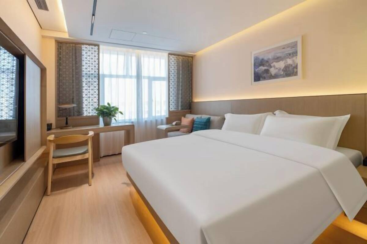 Ein Hotelzimmer mit Bett, Schreibtisch, Stuhl, Fernseher und einem Fenster mit Vorhängen.