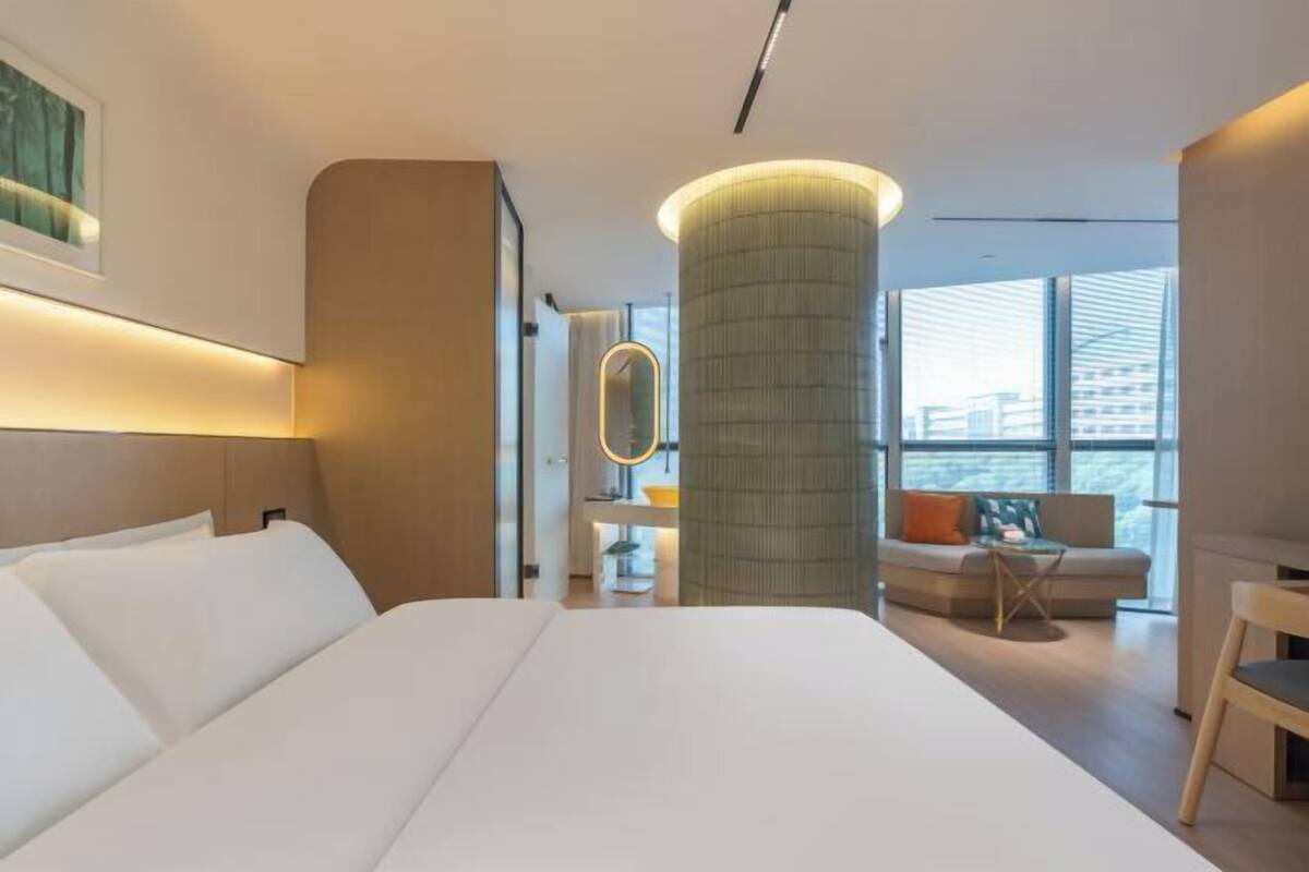Ein modernes Hotelzimmer mit einem großen Bett, einer runden Säule, einer Couch und Blick auf die Stadt.