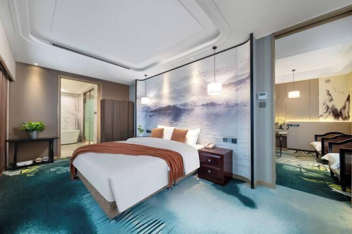 Ein Hotelzimmer mit Bett, Nachttisch und Blick auf das Meer durch ein großes Fenster.