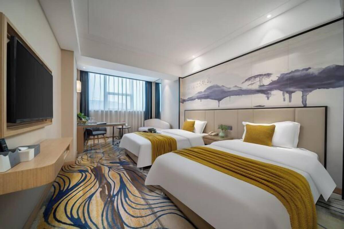 Ein Hotelzimmer mit zwei Betten, einem Schreibtisch, einem Stuhl, einem Fernseher und einem großen abstrakten Gemälde an der Wand.