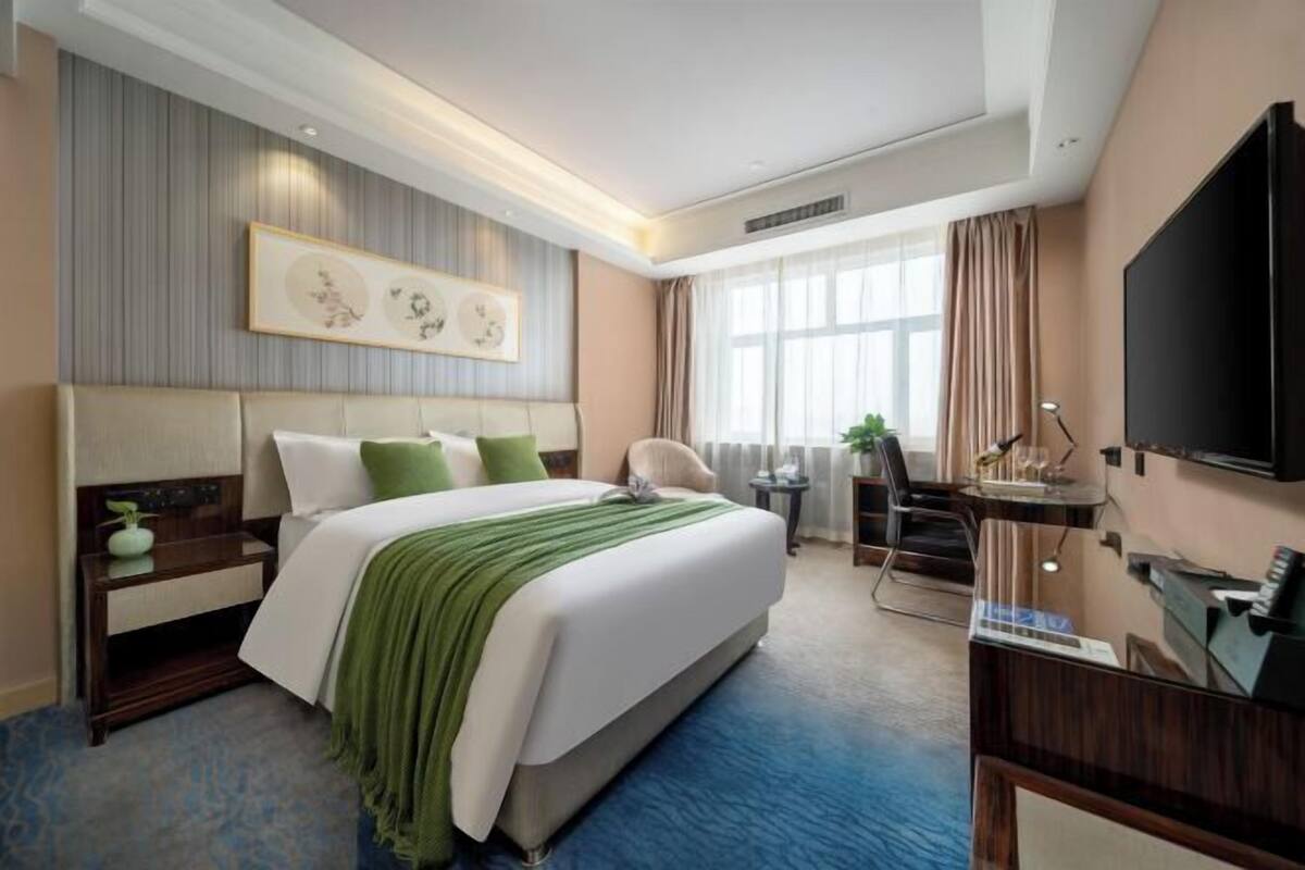 Ein Hotelzimmer mit einem großen Bett, einem Schreibtisch, einem Stuhl, einem Fernseher und einem Fenster mit Vorhängen.