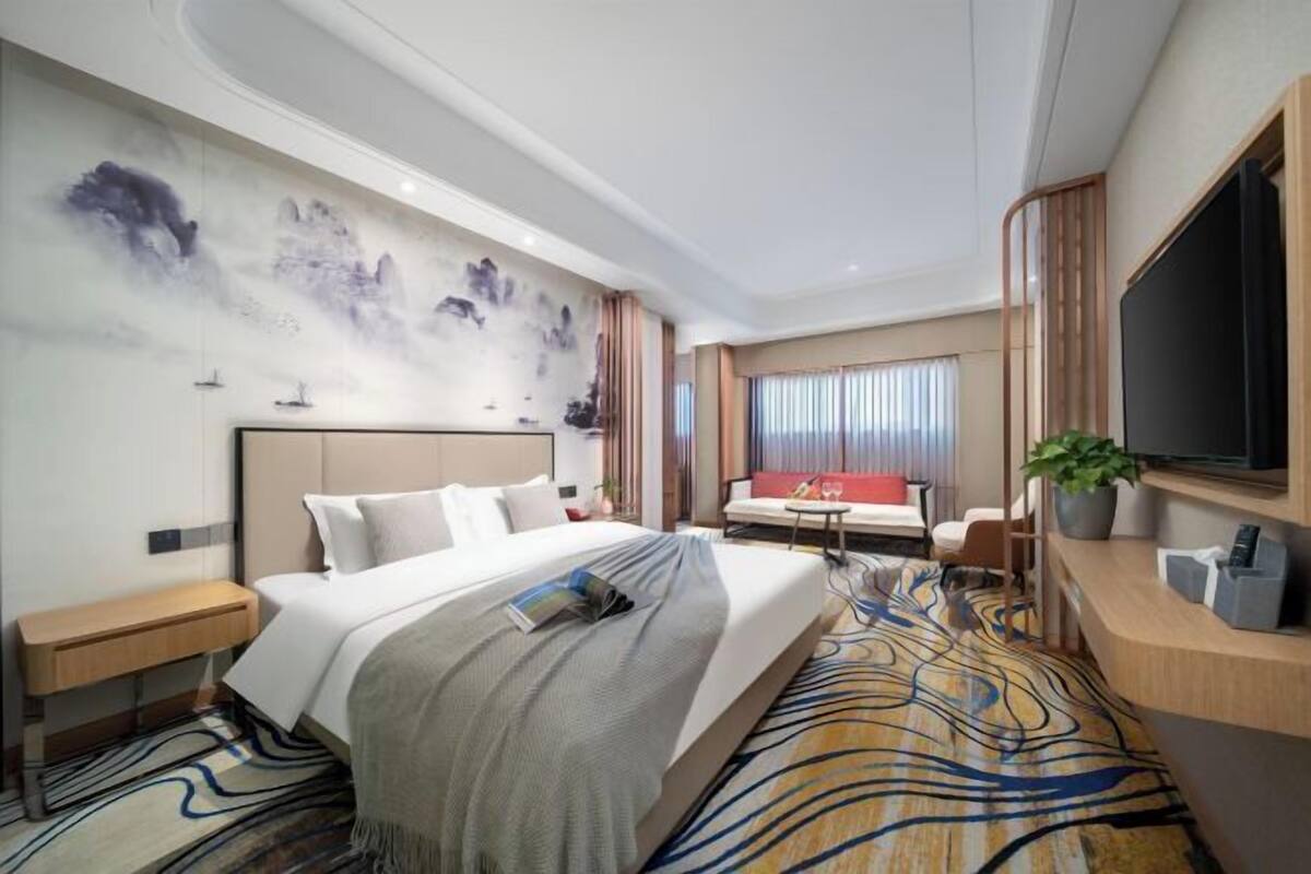 Ein Hotelzimmer mit Bett, Schreibtisch, Fernseher, Sofa und einem Wandbild.