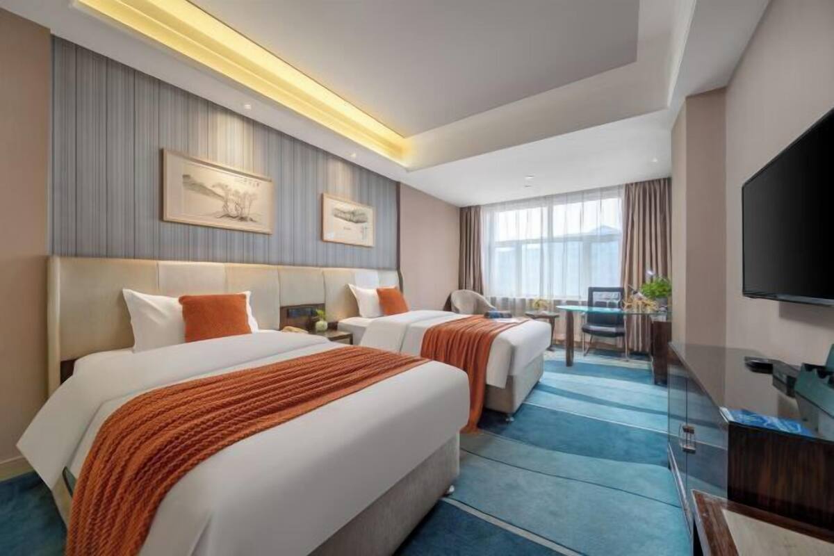 Ein Hotelzimmer mit zwei Betten, einem Schreibtisch, einem Flachbildfernseher und Kunstwerken an den Wänden.