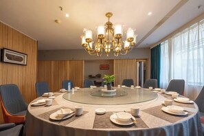 A conference room with a round glass table, blue chairs, a chandelier, and a potted plant. - Urumqi Yaxin Hotel (Degang Wanda Airport) (Urumqi)
