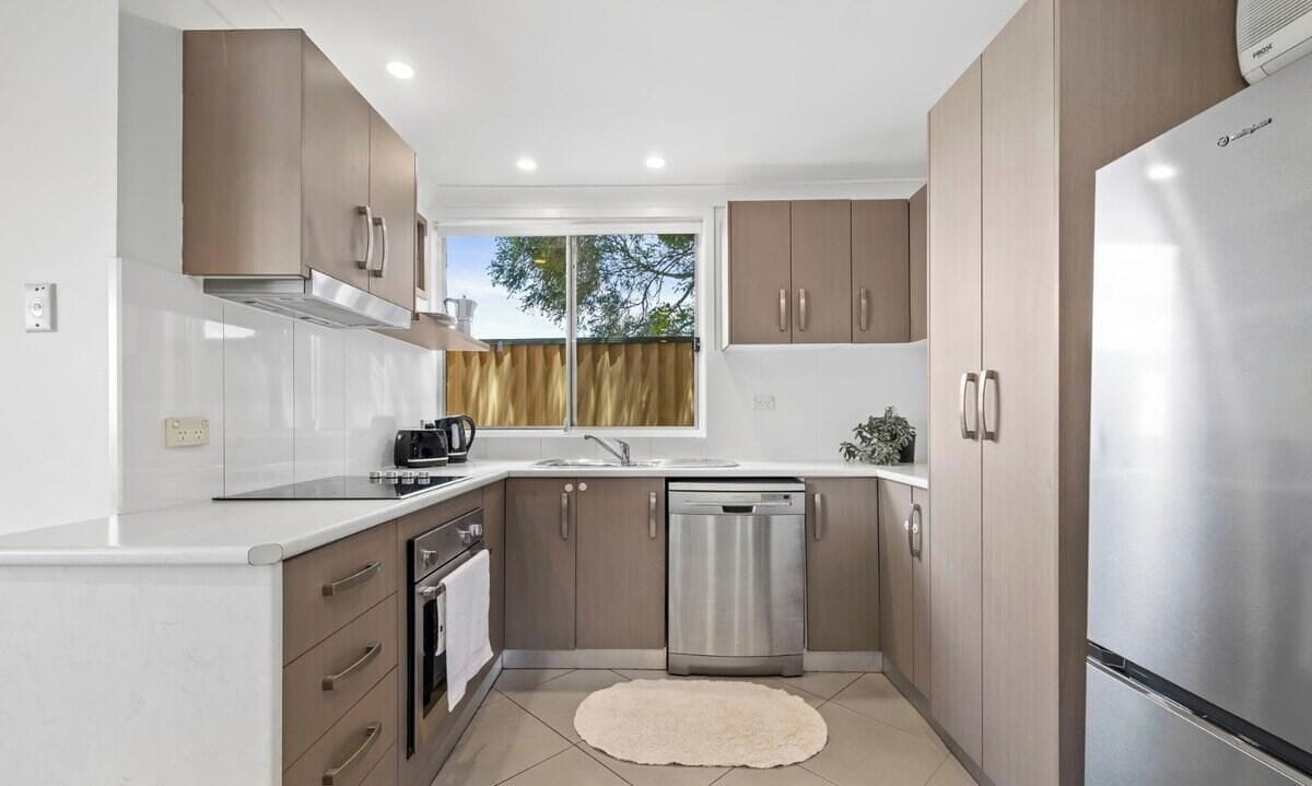 A modern kitchen with stainless steel appliances, wooden cabinets, and a large window.
