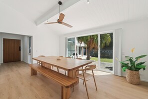 A spacious room with a large wooden table, a ceiling fan, and a sliding glass door leading to an outdoor area. - Hidden Gem, Sauna, Pet-Friendly! (Arrawarra Headland)