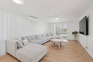 A modern living room with a sectional sofa, a round coffee table, and a flat-screen TV mounted on the wall. - Hidden Gem, Sauna, Pet-Friendly! (Arrawarra Headland)